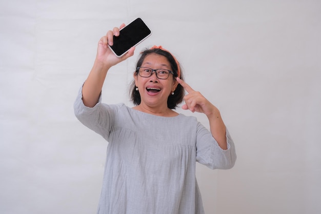 Una mujer asiática señalando el teléfono celular en su mano sonriendo expresión alegre