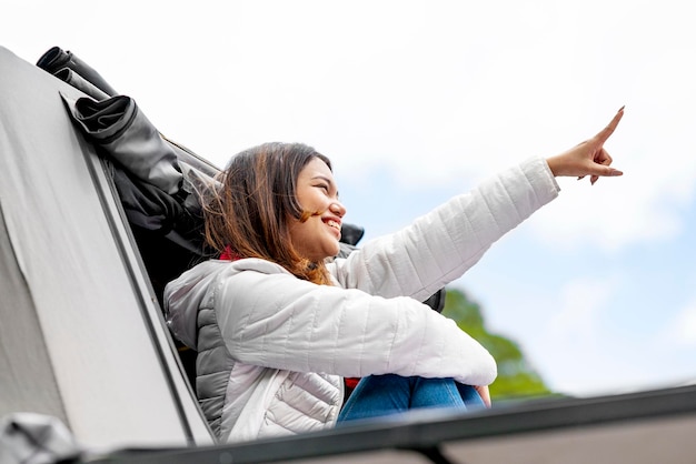 Mujer asiática sentada afuera de la carpa sobre la autocaravana y señalando algo