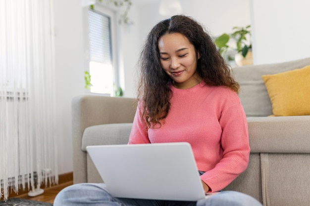 Mujer asiática sentada con una computadora en un sofá estudiando en casa elearning y concepto de trabajo independiente remoto