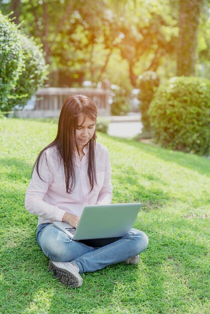 Mujer asiática sentada en un parque verde usando una computadora portátil