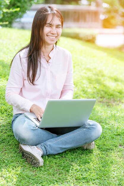 Mujer asiática sentada en un parque verde usando una computadora portátil