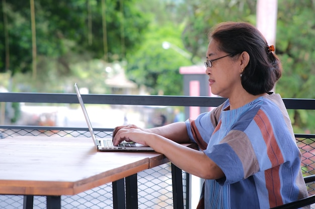 Foto mujer asiática sentada sola en la terraza de su casa trabajando en una computadora portátil en la mesa