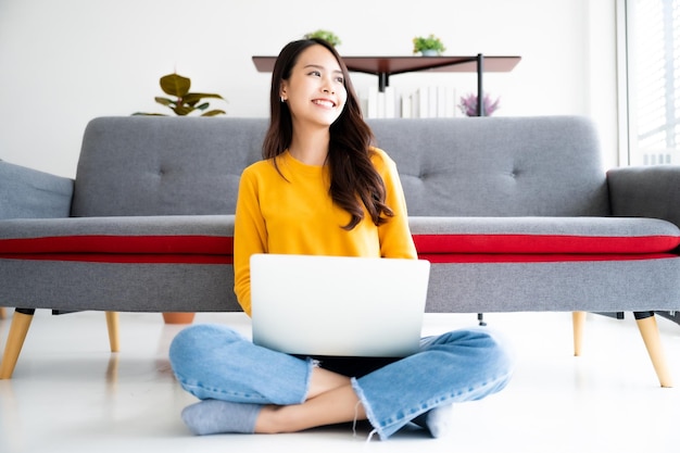 Mujer asiática sentada en el suelo y usando una computadora portátil