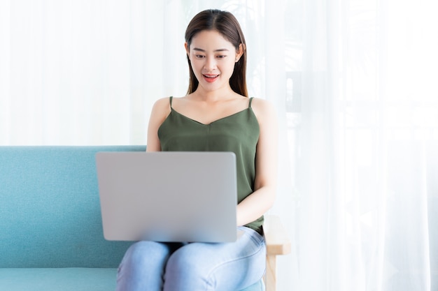 Mujer asiática, sentado, usar la computadora portátil, en, sofá