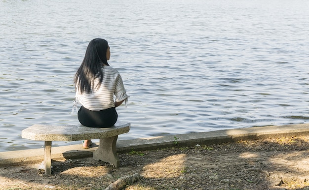 Mujer asiática en una silla que se sienta solamente en el fondo del río, del puente y del lago.