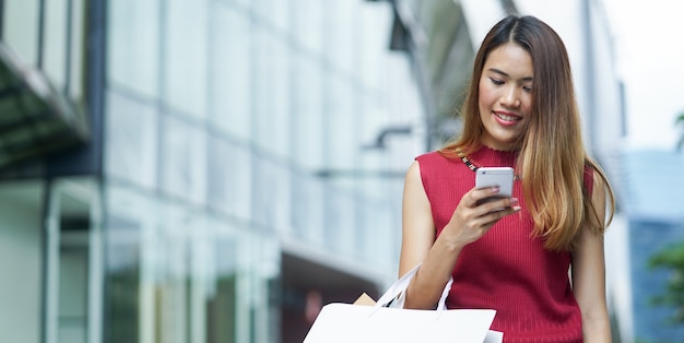 Foto mujer asiática con smartphone con bolsas de compras
