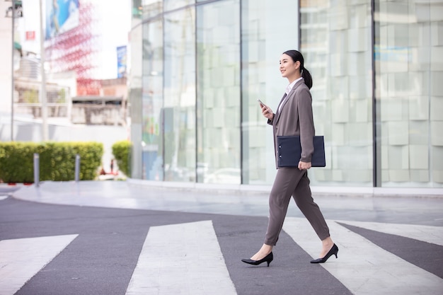 Mujer asiática con smartphone caminando por la calle edificio borroso