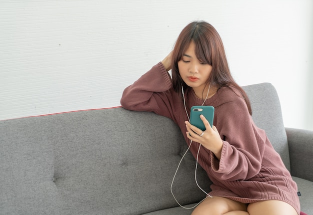 Mujer asiática con smartphone en sofá gris en sala de estar
