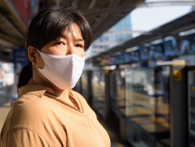 Mujer asiática con sobrepeso con máscara esperando en la estación de tren del cielo