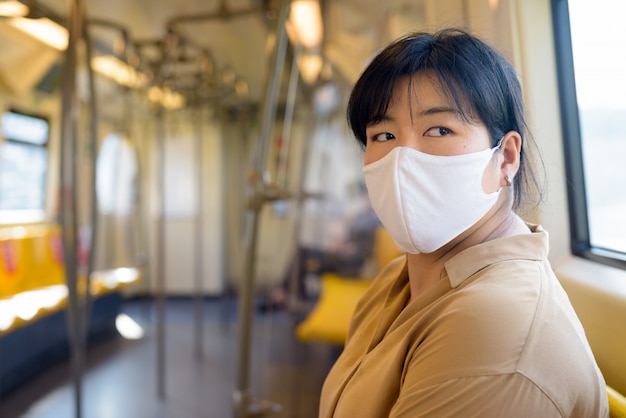 Mujer asiática con sobrepeso con máscara pensando mientras está sentado con distancia dentro del tren