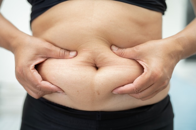 La mujer asiática con sobrepeso muestra el vientre gordo en la oficina.