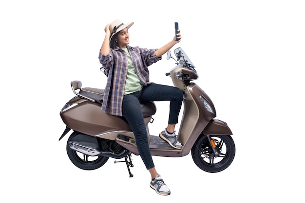 Una mujer asiática con sombrero está sentada en una moto y tomando un autorretrato con un teléfono móvil