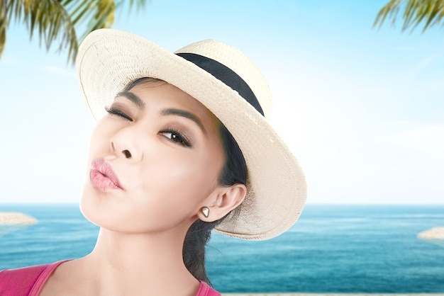 Mujer asiática con sombrero haciendo selfie en la playa con vista al cielo azul