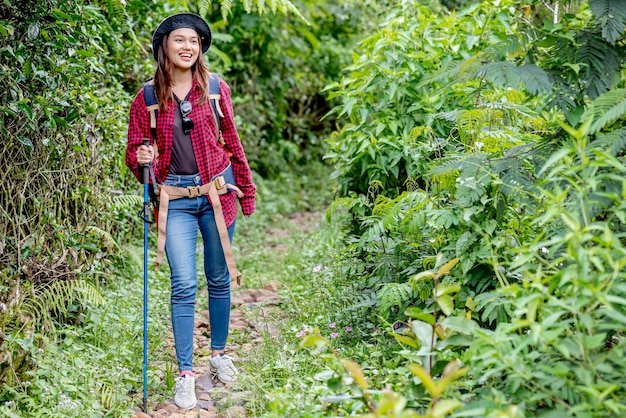 Mujer asiática con sombrero y mochila con bastón de trekking.