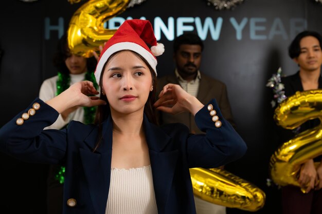 Mujer asiática con un sombrero de Papá Noel con globos de oro en el fondo en una fiesta de Año Nuevo