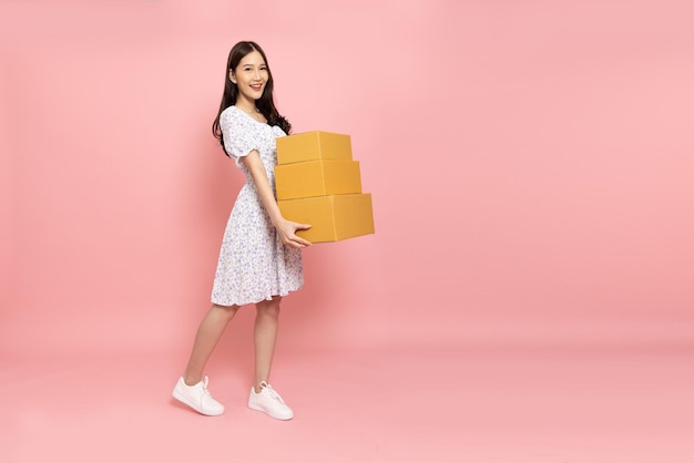 Foto mujer asiática sonriendo y sosteniendo una caja de paquetes aislada en un fondo rosa