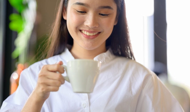 Mujer asiática sonriendo y tomando café en la cafetería