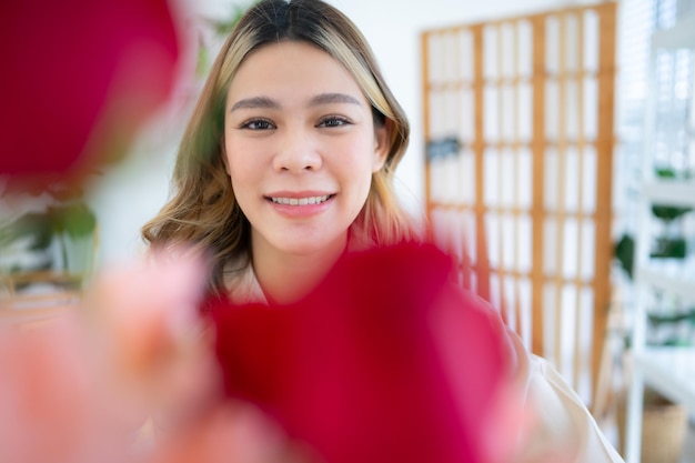 Una mujer asiática sonriente con una flor rosa en la mano en casa.