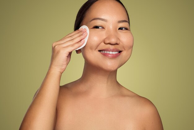 Mujer asiática sonriente limpiando la cara con una almohadilla de algodón