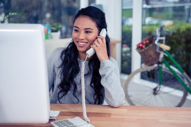 Mujer asiática sonriente en llamada de teléfono en oficina