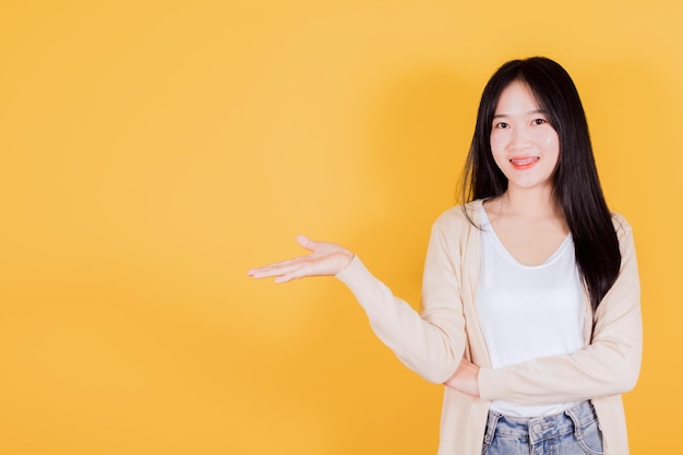 Mujer asiática sonriente mano abierta vacía sobre fondo amarillo