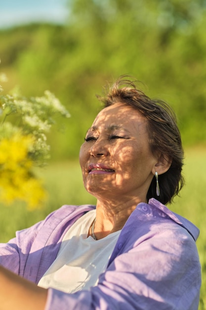Mujer asiática sonriente de mayor edad en un parque de verano con flores silvestres, el video transmite un