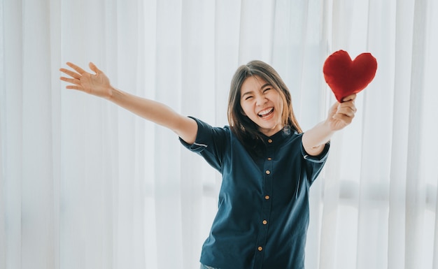 Mujer asiática sonriente que muestra el corazón rojo con los brazos abiertos