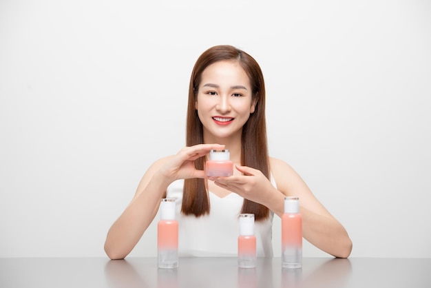Mujer asiática sonriente que muestra productos cosméticos para el cuidado de la piel