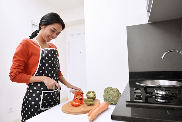 Mujer asiática sonriente que usa el cuchillo para cortar pimientos y cocinar