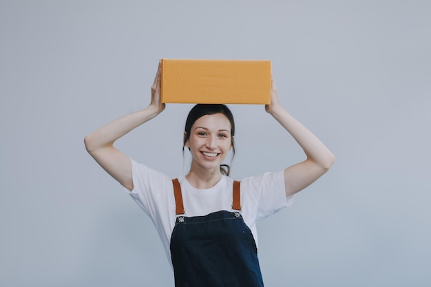 Mujer asiática sonriente con ropa casual sosteniendo una maqueta de caja de cartón mientras está de pie contra un concepto de negocio de envío de fondo blanco aislado