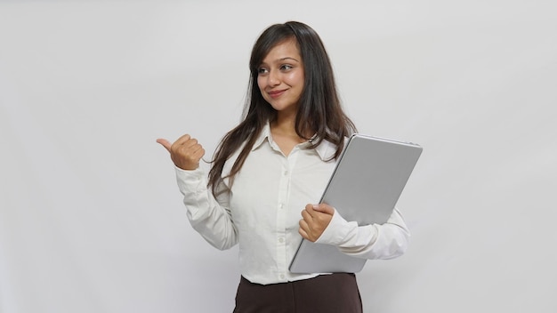 Mujer asiática sonriente con ropa de negocios sosteniendo una laptop y señalando