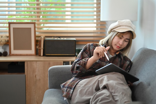 Mujer asiática sonriente sentada en el sofá y usando una tableta digital