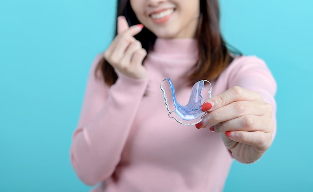 Mujer asiática sonriente sosteniendo un retenedor de ortodoncia en el fondo de la pantalla azul. Cuidado dental y dientes sanos.