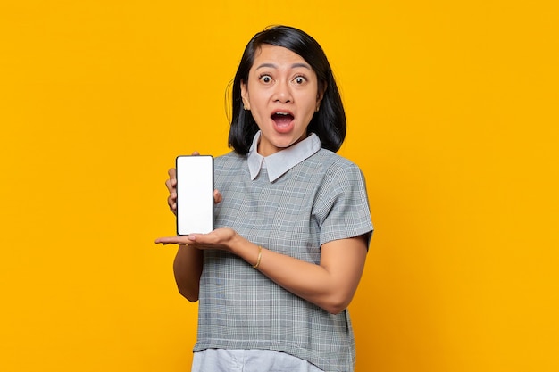 Mujer asiática sorprendida que muestra la pantalla del smartphone en blanco con la palma. concepto de promoción de productos