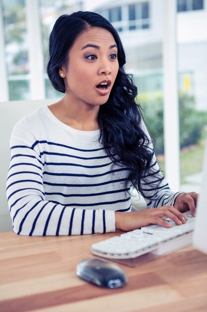 Mujer asiática sorprendida usando la computadora en la oficina