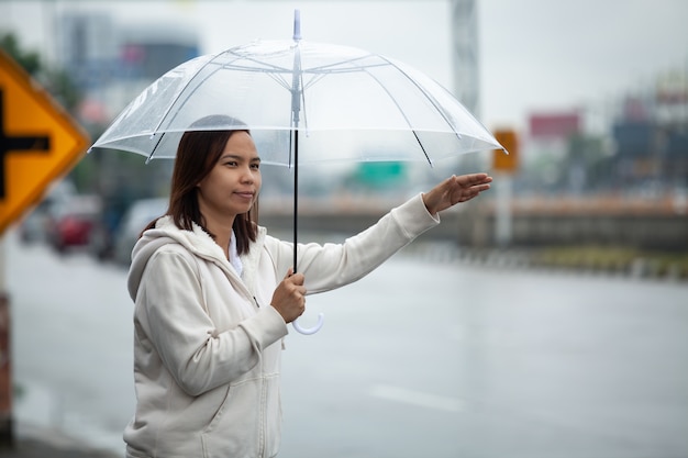 Foto mujer asiática sosteniendo paraguas haciendo autostop en taxi en las calles de la ciudad en el día lluvioso.