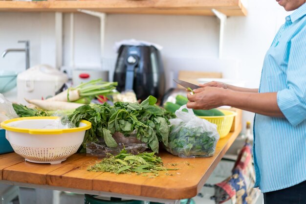 La mujer asiática sostiene un cuchillo y prepara muchas verduras para cocinar en la cocina trasera