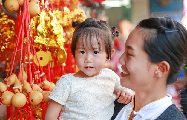 La mujer asiática y su hija en vestido chino contra decoraciones rojas chinas tradicionales