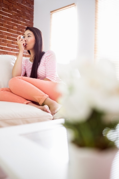 Mujer asiática con su inhalador en el sofá