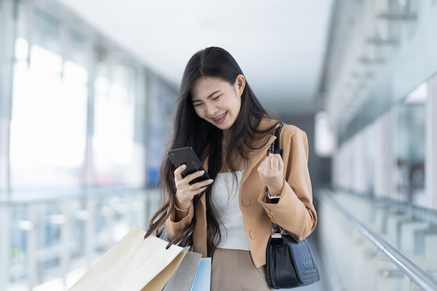 Mujer asiática sube al ascensor y juega con su teléfono móvil para comprar en el centro comercial