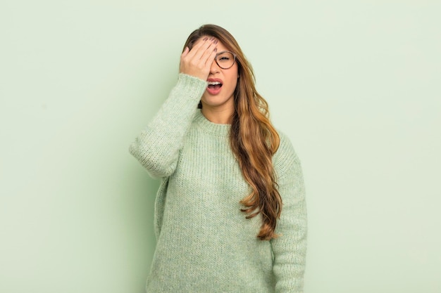 Mujer asiática con sueño, aburrida y bostezando con dolor de cabeza y una mano cubriendo la mitad de la cara