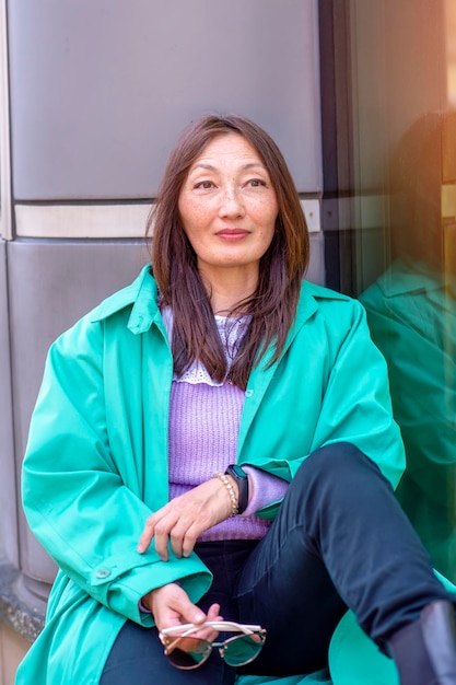 Mujer asiática con suéter morado y trinchera verde caminando por la ciudad europea y usando el teléfono