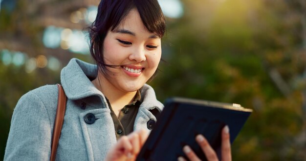 Mujer asiática tableta y ciudad para investigación de redes sociales o comunicación en redes al aire libre Cara de persona femenina feliz sonrisa en la tecnología para búsqueda en línea chatear o enviar mensajes de texto en una ciudad urbana