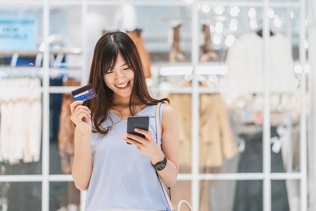 Mujer asiática con tarjeta de crédito con teléfono móvil para compras online en grandes almacenes