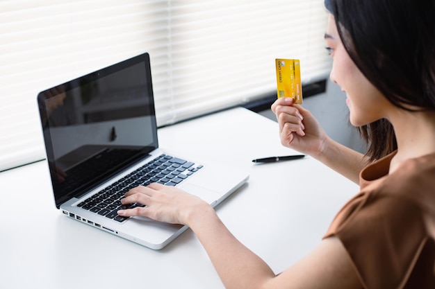 Mujer asiática con tarjeta de crédito y usando el concepto de compras en línea de una computadora portátil