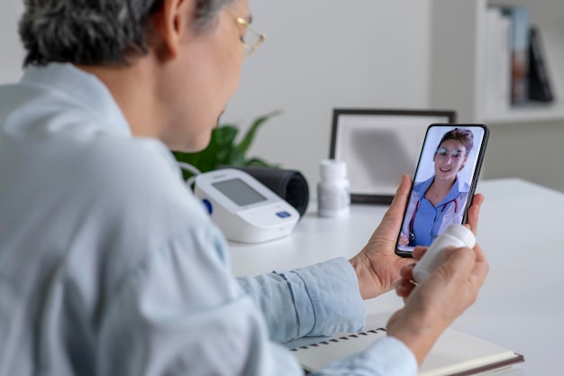 Foto mujer asiática con teléfono inteligente durante una consulta en línea con su médico en el concepto de telemedicina de su sala de estar