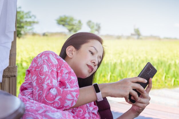 Mujer asiática con teléfono inteligente mientras está acostado sobre un cojín con vista a la naturaleza