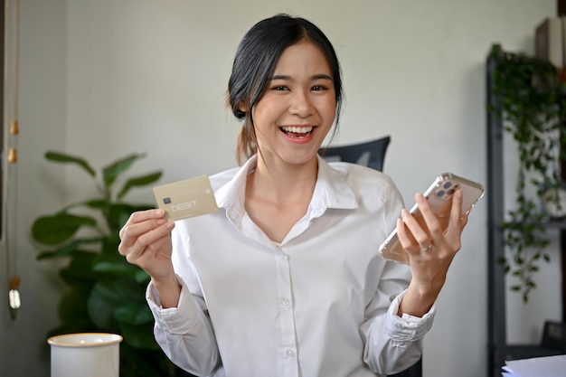 Una mujer asiática con un teléfono inteligente y una tarjeta de crédito comprando en línea