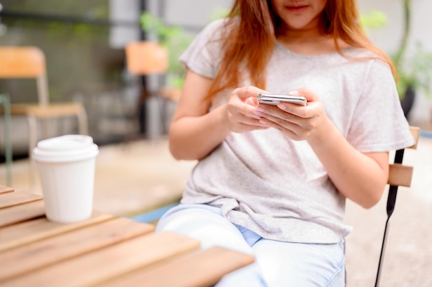 Mujer asiática con teléfono móvil y café sola. Relax y recreación en el jardín botánico de vacaciones.