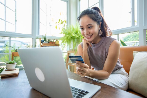 La mujer asiática tiene tarjeta de crédito y usa compras en línea desde el teléfono inteligente en casa.